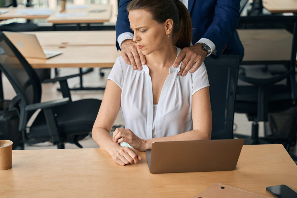 female looking uncomfortable while a superior rests his hand on her shoulders